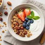 A bowl of vanilla nut granola served with yogurt, fresh fruit, and a sprig of mint