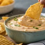 A close-up of a crispy chip dipping into a creamy dip.