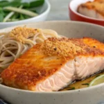 Delicious crispy salmon fillets served with soba noodles, garnished with green onions and sesame seeds, offering a healthy and flavorful meal.