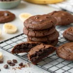 Freshly baked brownie box mix with bananas cookies on a cooling rack, showcasing their soft, chocolatey texture with a few chocolate chips and banana slices nearby.