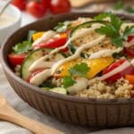 Colorful quinoa salad with roasted vegetables (zucchini, bell peppers, and tomatoes) topped with a creamy lemon tahini dressing and fresh parsley, perfect for a healthy meal.